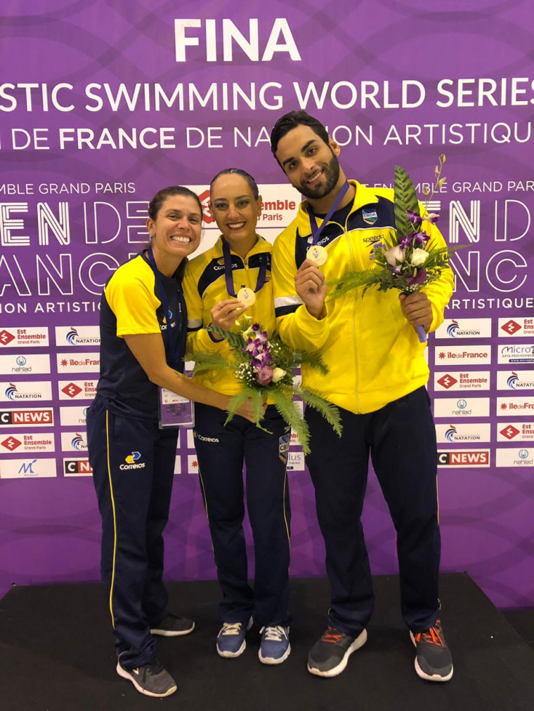 Giovana Stephan e Renan Alcântara recebem o ouro ao lado da técnica Roberta Perillier Giovana Stephan e Renan Alcântara recebem o ouro ao lado da técnica Roberta Perillier